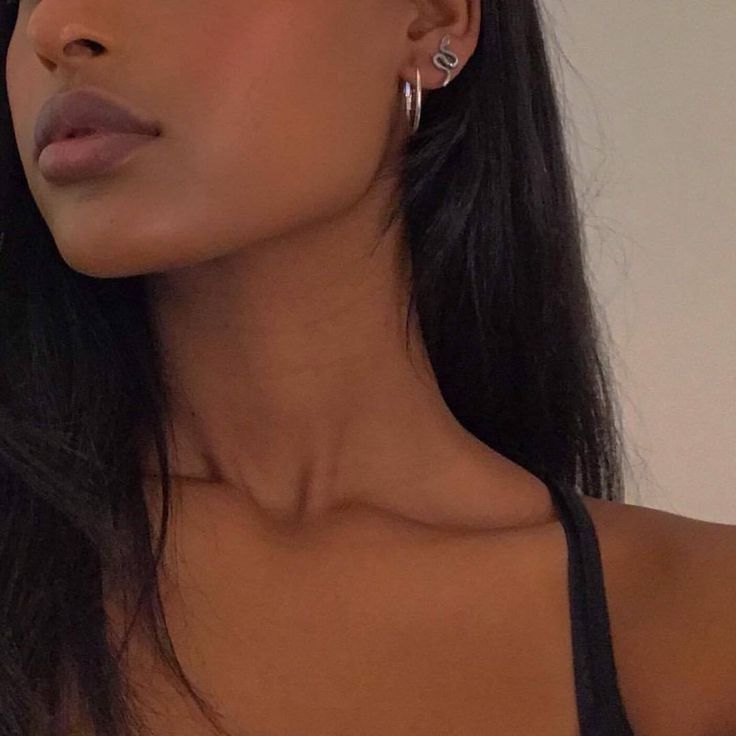 Side profile close-up of a woman with dark hair, showing her neck and jawline, wearing layered silver earrings and a black top.