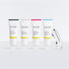 Four white tubes of ZIIP skincare gels lined up on a light gray reflective surface, with a small silver pump bottle resting to the right. The tubes are labeled Firm Gel, Glow Gel, Refresh Gel, and Clear Gel, each with a different colored accent band (black, gray, pink, and blue).