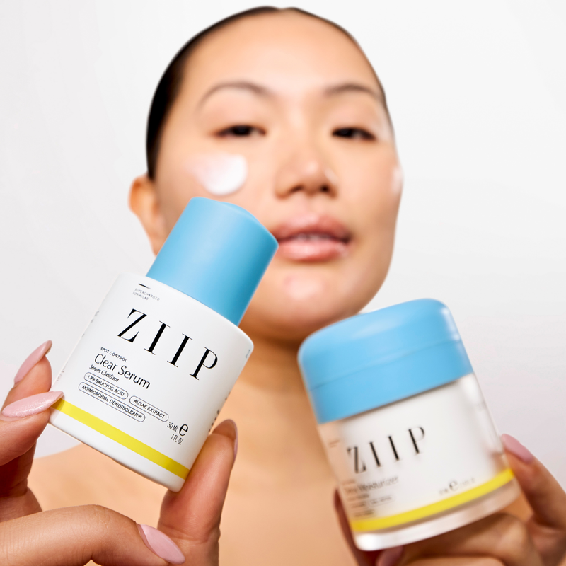 Woman holding ZIIP Clear serum and Detox moisturizer bundle with product applied to cheek